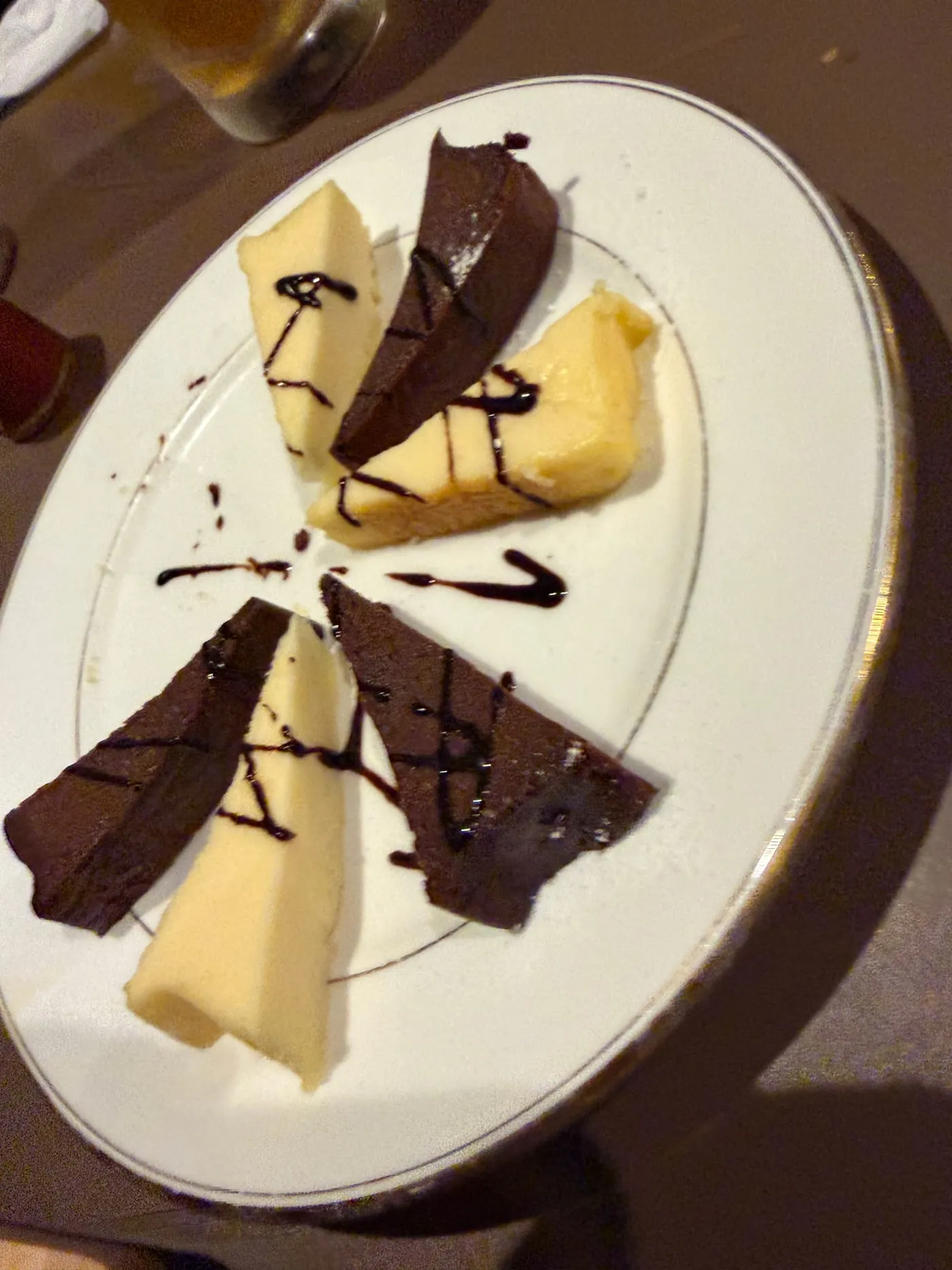白い丸皿に盛られたデザート。チョコレート色のケーキと淡い黄色のケーキが細い三角形に切られ、交互に放射状に並べられて、チョコレートソースで線が描かれている